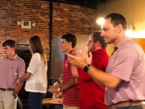 Group of people standing in room in front of brick wall.