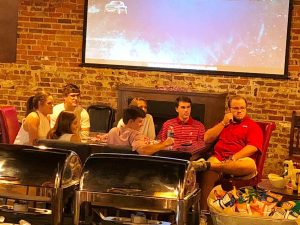 Group fo people sitting at table with white screen and brick wall.