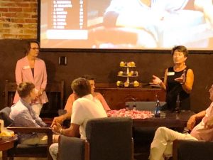 Group of people sitting in room with white screen in background.