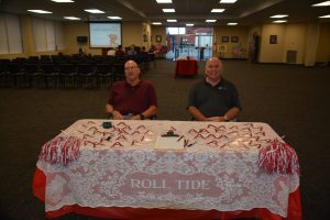 Two men sitting behind table with red and white cloth.