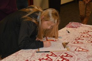 Lady signing paper at red and white table.