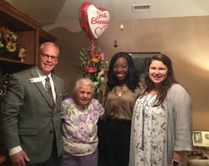 Alex Smith and Kayla White with two ladies with balloon in beige room.