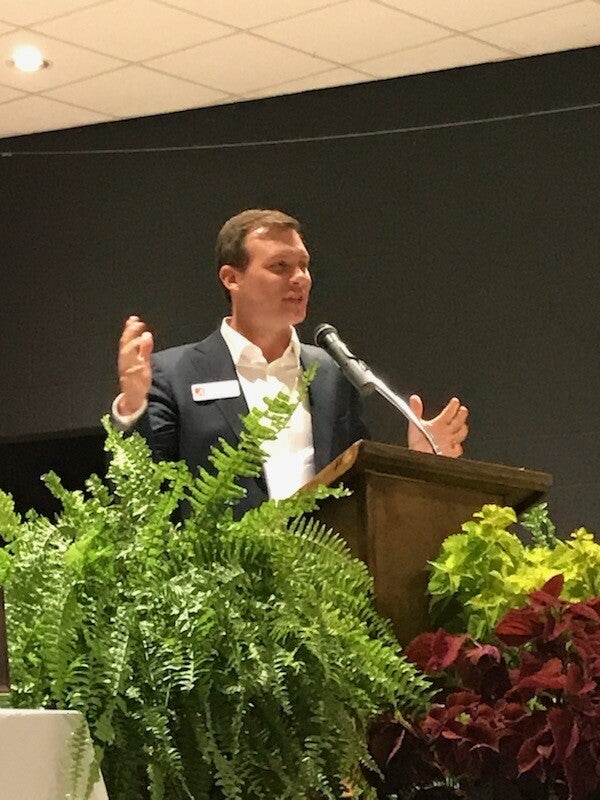 man standing behind podium and fern in front of podium