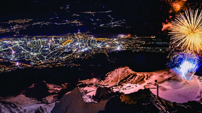 Fireworks exploding over a mountain at night with a lit city below