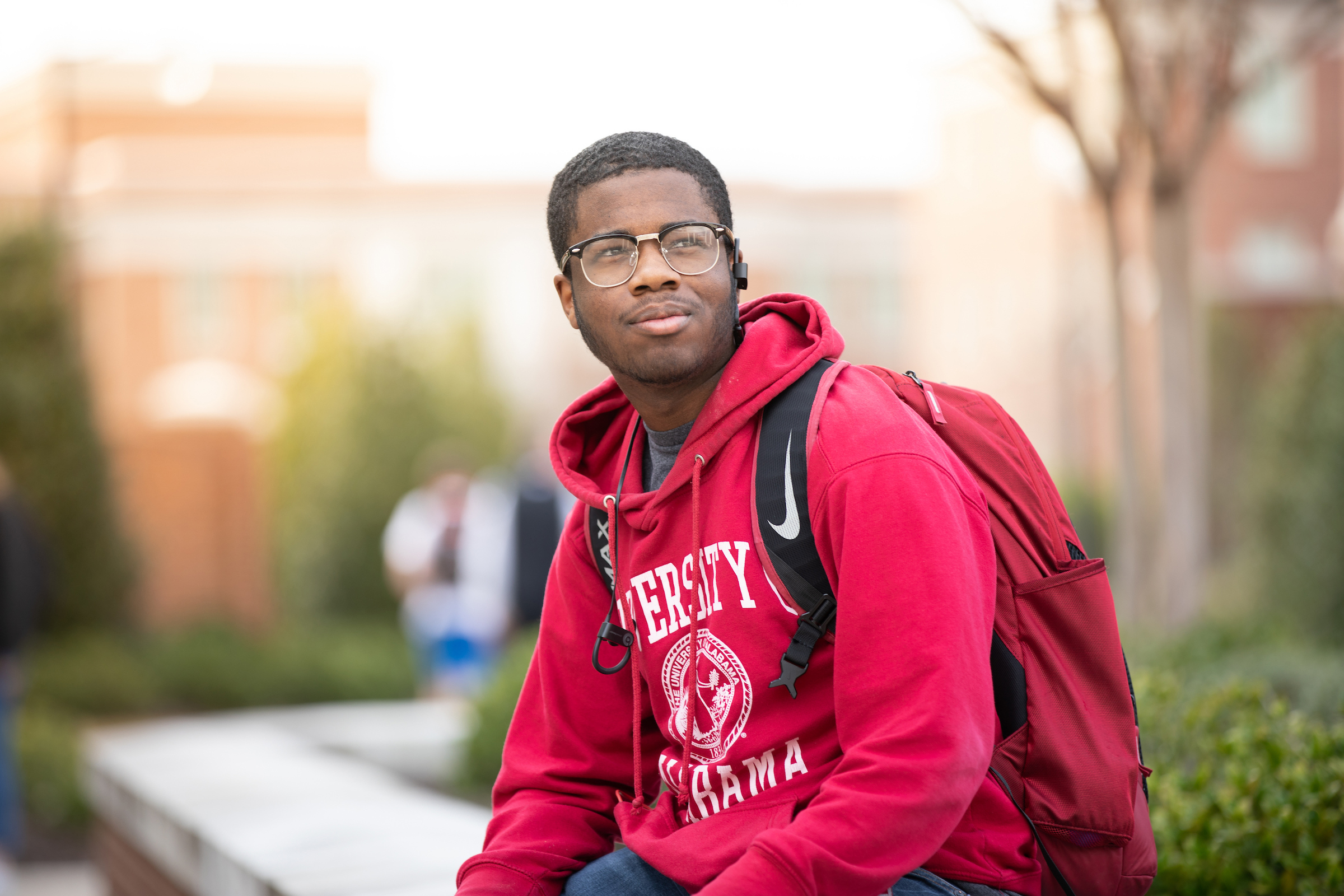 A UA student sitting on campus wearing a crimson UA sweatshirt