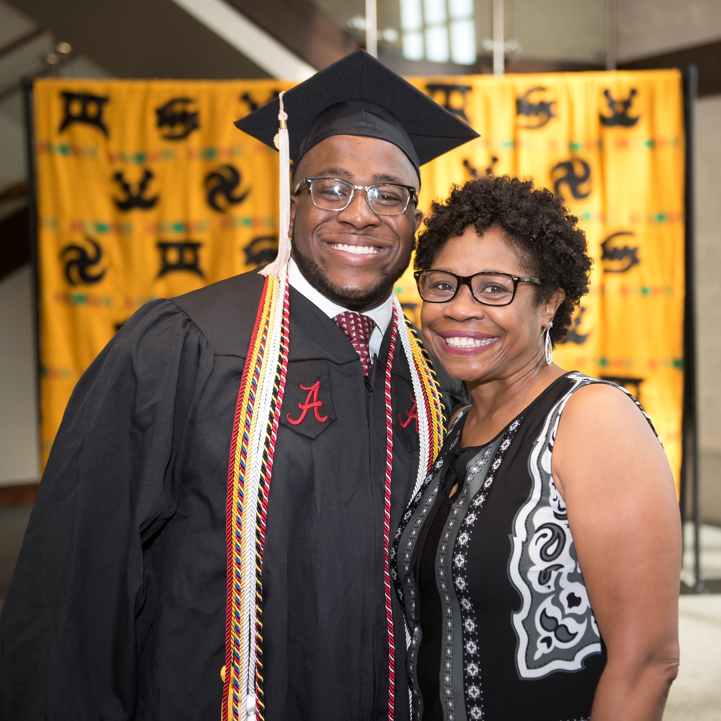 UA graduate in cap and gown standing next to his mother