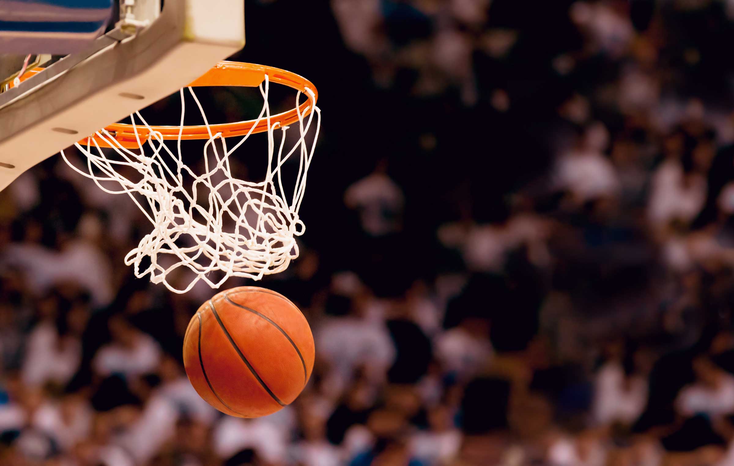A basketball just passing through the net at a crowded indoor basketball game